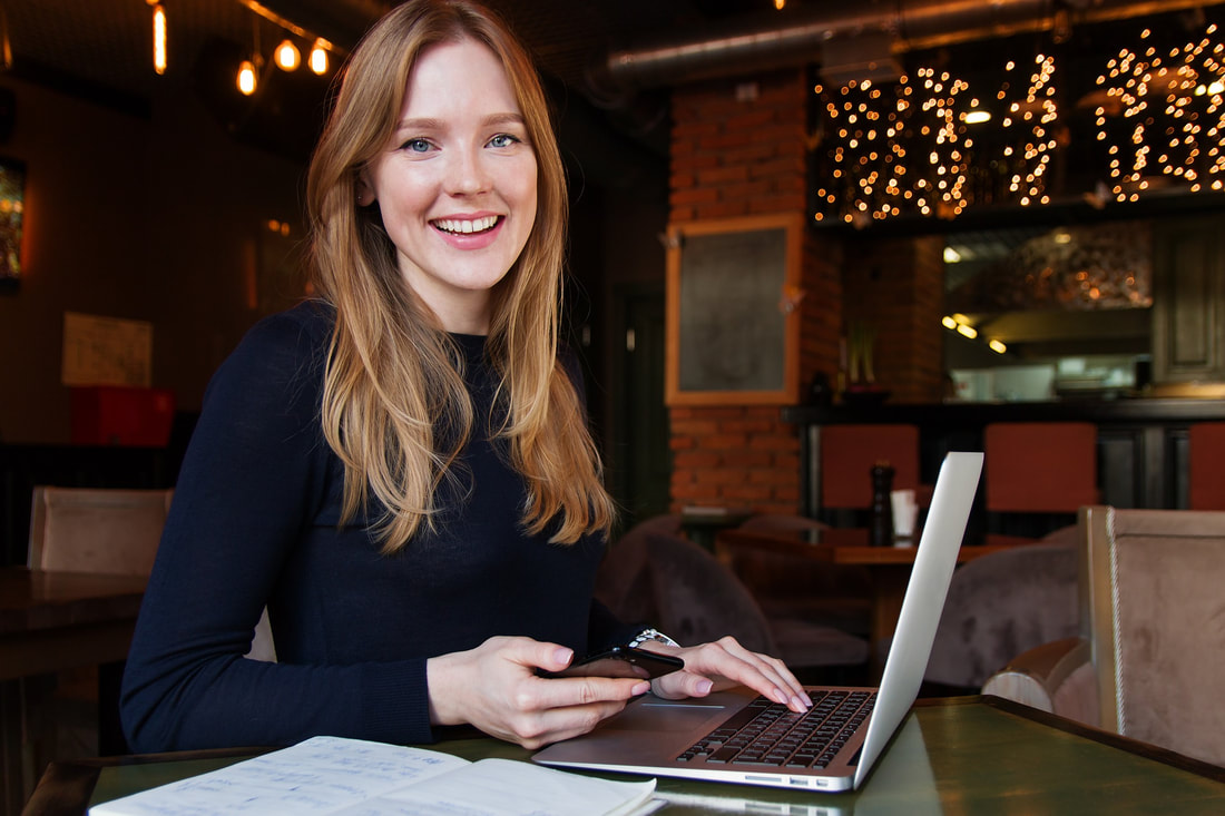 Woman sitting at laptop and holding phone in cafe