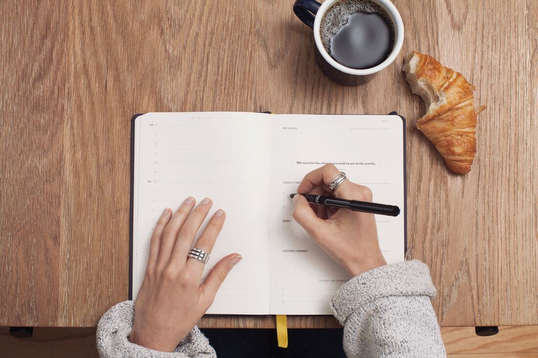 woman's hands writing content in journal with coffee and pastry 