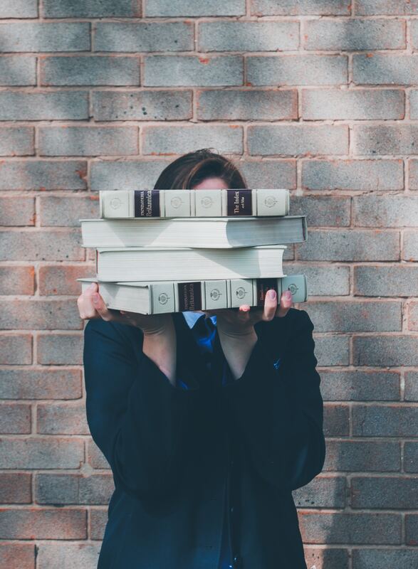 entrepreneur holding stack of books in front of her face 