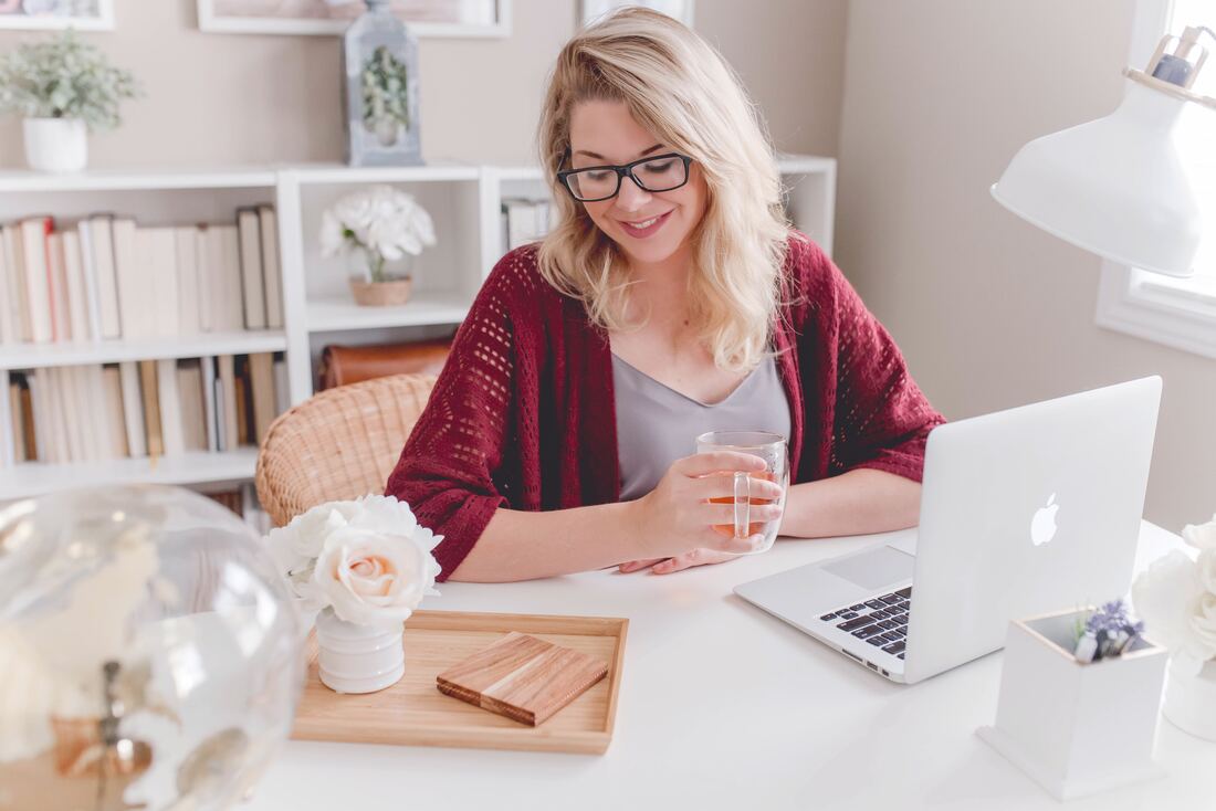 Female entrepreneur smiling holding glass mug sitting beside table with MacBook